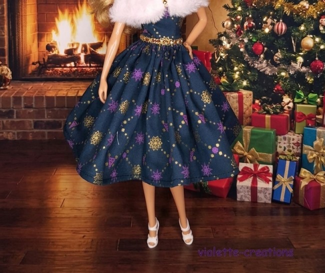 Poupée Barbie portant une robe de Noël bleu saphir avec motifs dorés et violets, accompagnée d'une étole en fausse fourrure blanche