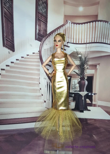 Poupée Barbie portant une robe de gala coupe sirène en tissu métallisé doré avec une traîne en tulle pailleté