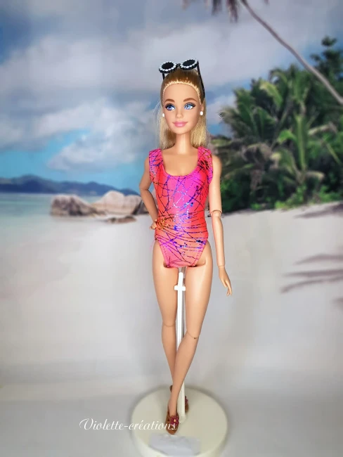 Maillot de bain 1 pièce graphique rose et orange pour poupée mannequin type barbie (2) Maillot de bain 1 pièce en lycra rose et orange à motifs graphiques sur une poupée mannequin blonde avec lunettes de soleil, devant un fond de plage tropicale.