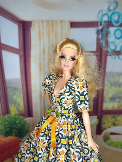 Robe de galla longue pour poupée type Barbie en coton, motif mosaïque géométrique vert émeraude et ocre sur fond écru, décolleté V, manches bouffantes, blason doré et ruban de velours ocre à la taille, création artisanale par Violette-Creations.