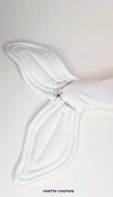 Barbie portant une tenue de sirène blanche scintillante avec effet strass et un haut assorti en forme de coquillage, posé sur un décor de plage