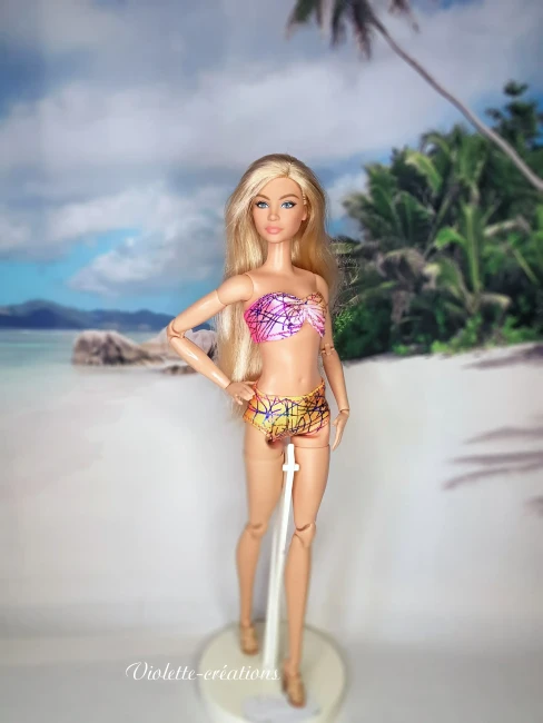 Maillot de bain 2 pièces graphique pour poupée mannequin type barbie (2) Maillot de bain 2 pièces en lycra multicolore aux motifs graphiques sur une poupée mannequin blonde de 29 cm, avec un fond de plage tropicale.