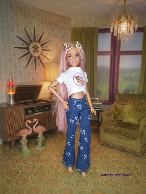 Poupée Barbie portant un jean bleu à cœurs, un maillot rose fushia, un blouson violet décoré de papillons et un t-shirt à motif sous le blouson.