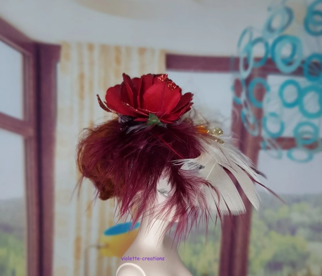 Chapeau bibi rouge pour poupée type barbie avec rose à paillettes, plumes bordeaux et blanches, et ornement doré.