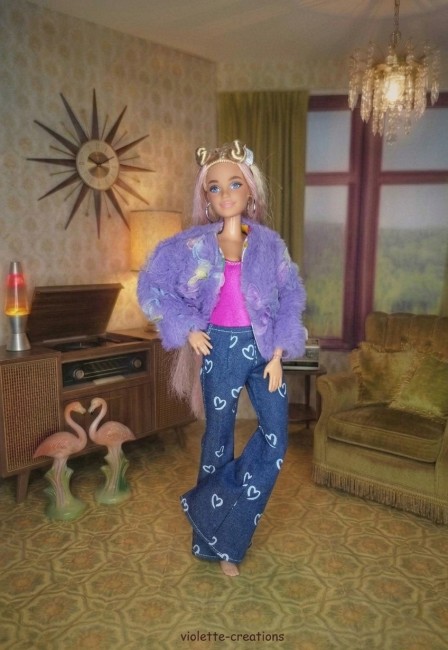 Poupée Barbie portant un jean bleu à cœurs, un maillot rose fushia, un blouson violet décoré de papillons et un t-shirt à motif sous le blouson.