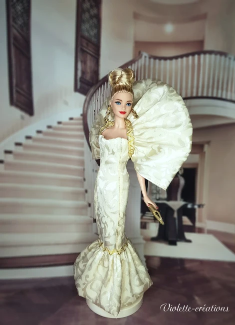 Poupée Barbie de collection en robe de soirée sirène dorée et argentée, posant dans un salon de luxe feutré avec chandeliers.