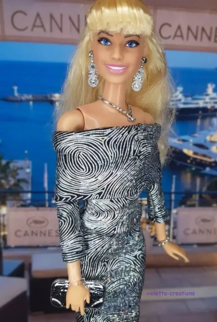 Robe de cocktail argentée pour poupée mannequin, style fourreau à motifs tourbillonnants, création Violette-Creations sur fond de soirée de gala à Cannes