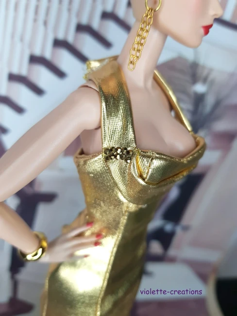 Gros plan sur le bustier plissé et les détails de bretelles avec strass d'une robe de soirée dorée pour poupée Barbie