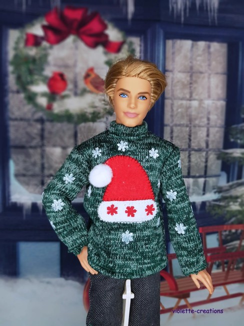 Poupée mannequin Ken portant un pull vert décoré d’un bonnet rouge et de flocons de neige scintillants.