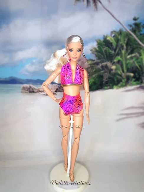 Maillot de Bain 2 Pièces Rose et Or pour Poupée Mannequin type Barbie Poupée mannequin type Barbie portant un maillot de bain 2 pièces bicolore rose et orange avec bordure dorée, posant sur une plage de sable fin avec palmiers et fleurs tropicales, par Violette-créations