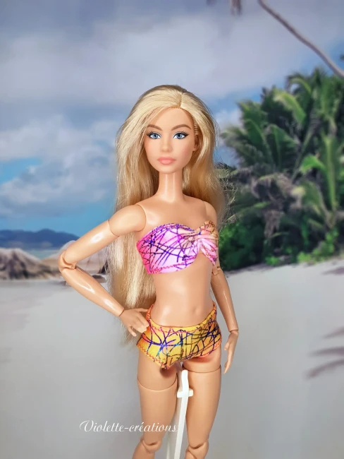 Maillot de bain 2 pièces graphique pour poupée mannequin type barbie (3) Maillot de bain 2 pièces en lycra multicolore aux motifs graphiques sur une poupée mannequin blonde de 29 cm, avec un fond de plage tropicale.