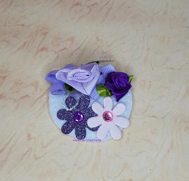 Chapeau bibi lilas pour poupée type barbie avec roses en ruban, fleurs pailletées et perles blanches.