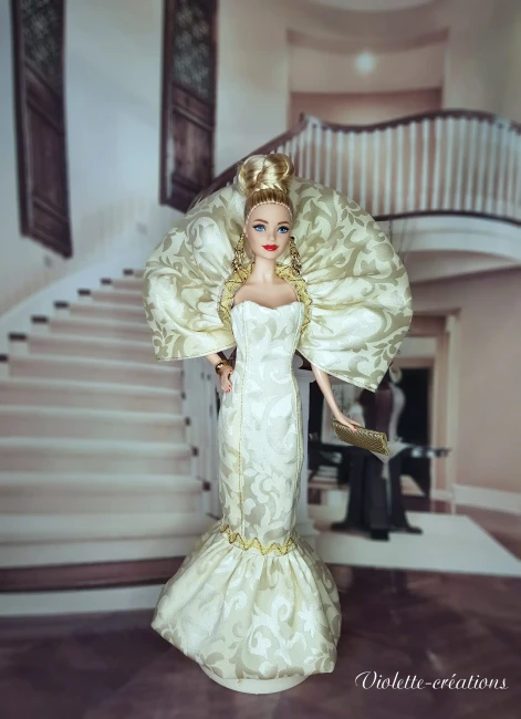 Poupée Barbie de collection en robe de soirée sirène dorée et argentée, posant dans un salon de luxe feutré avec chandeliers.