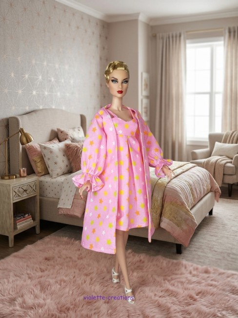 Ensemble Nuit Poupée Barbie : Nuisette Rose et Peignoir Étoiles Poupée Barbie portant un ensemble de nuit rose avec motif étoiles jaunes et blanches, incluant une robe de chambre à volants.