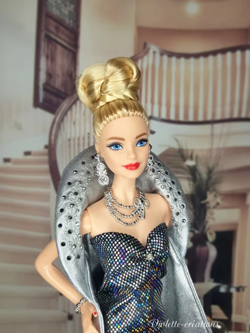 Poupée barbie portant une robe de soirée longue à paillettes avec cape argentée, dans un décor de grand escalier luxueux