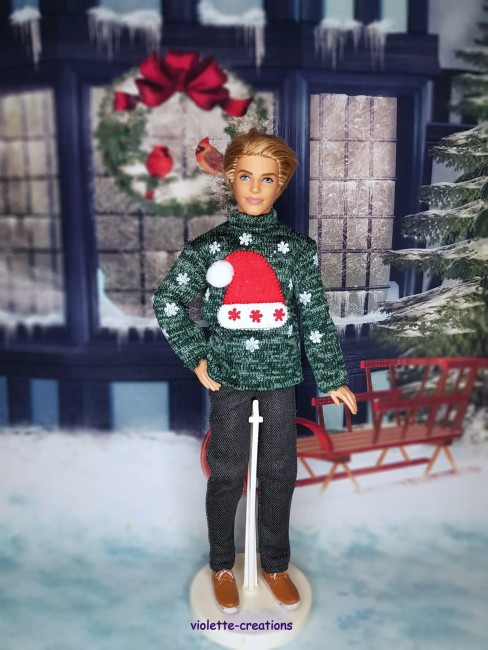 Poupée mannequin Ken portant un pull vert décoré d’un bonnet rouge et de flocons de neige scintillants.