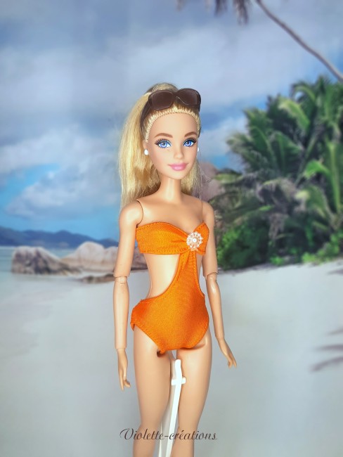 Maillot de bain 2 pièces pour poupée mannequin type Barbie – Look plage tropical Poupée mannequin type Barbie portant un maillot de bain 2 pièces orange sur une plage tropicale avec palmiers.