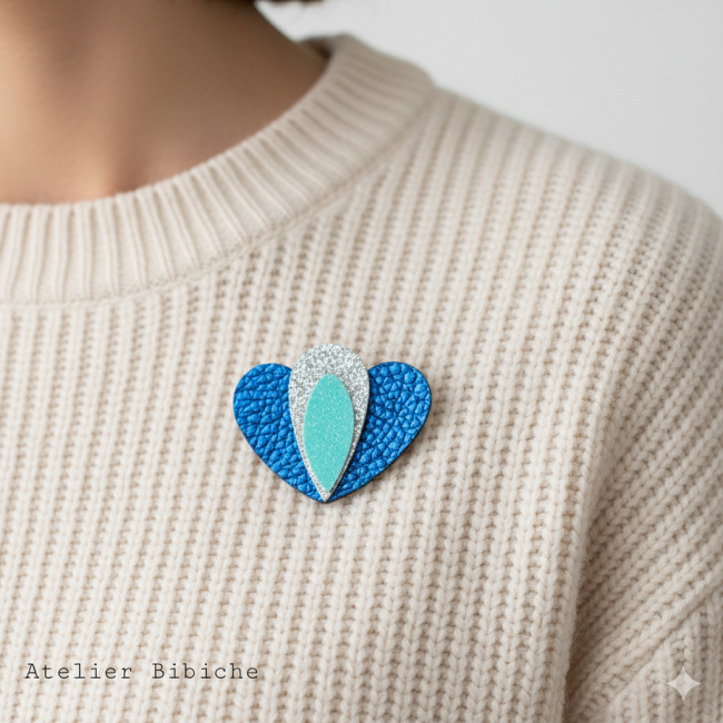Broche Cœur Lotus Fait Main - Bleu, Turquoise Pailleté Broche en forme de cœur bleu cobalt métallisé, avec un motif central en forme de pétale de lotus, argent pailleté et turquoise pailleté.