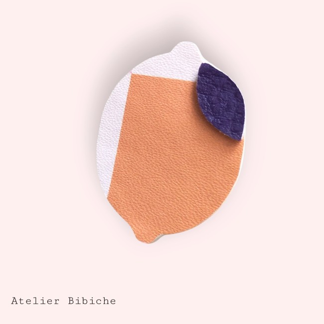Broche en forme de citron stylisé, motif bicolore orange pêche et blanc, avec une feuille en simili-cuir violet.