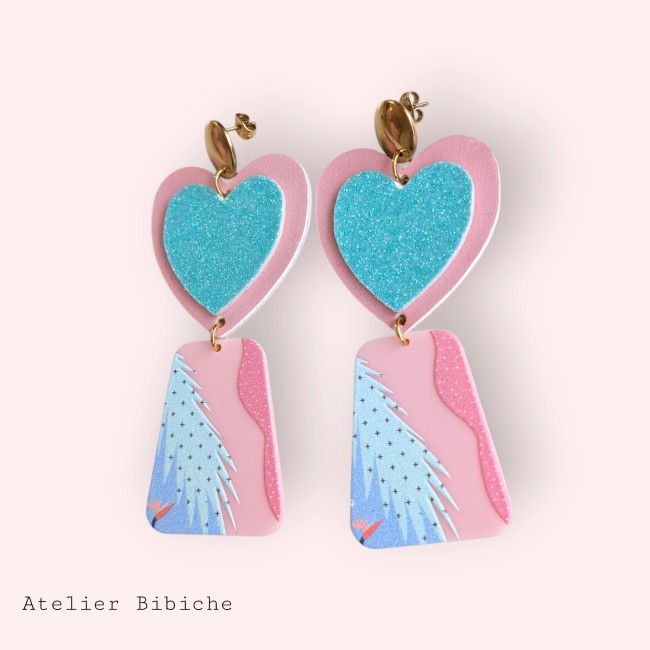Boucles d'Oreilles Coeur Turquoise & Sapin Noël - Atelier Bibiche Boucles d'oreilles longues, pendantes, avec un cœur rose et turquoise pailleté et un motif graphique de sapin de Noël stylisé sur fond rose.