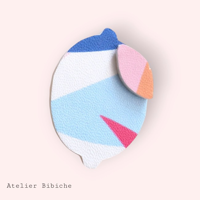 Broche en forme de citron stylisé, motif abstrait géométrique bleu et blanc, avec une feuille rose et orange.
