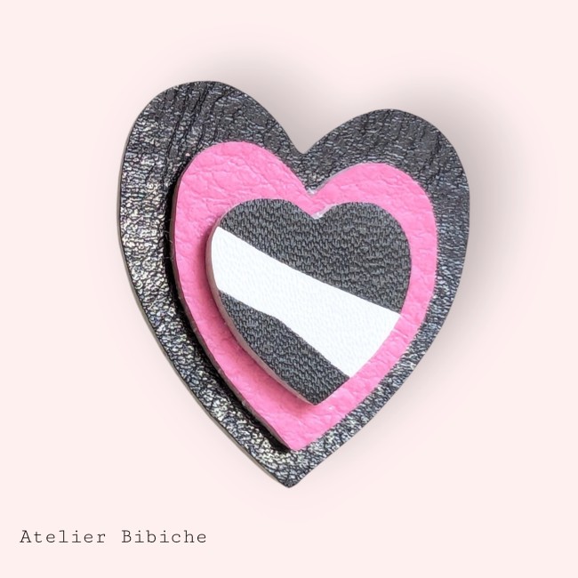 Broche cœur triple couche : extérieur noir, milieu rose néon et cœur intérieur rayé noir et blanc.