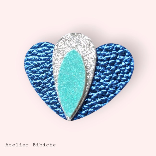 Broche Cœur Lotus Fait Main - Bleu, Turquoise Pailleté Broche en forme de cœur bleu cobalt métallisé, avec un motif central en forme de pétale de lotus, argent pailleté et turquoise pailleté.