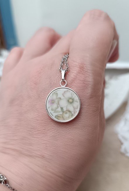 Collier en porcelaine ancienne présenté en main pour apprécier son pendentif rond de 18 mm plaqué argent.