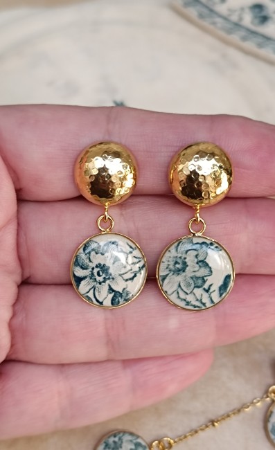Boucles d'oreilles présentées en main pour apprécier les dimensions et les détails du décor d'origine.