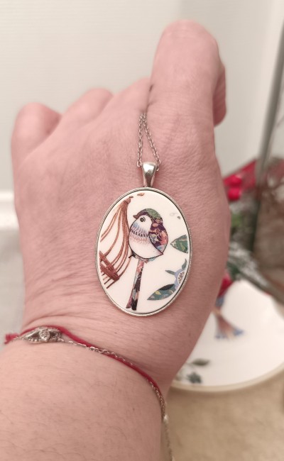Collier À la Volette – Tenue en main Collier À la Volette tenu dans la main pour montrer la finesse du pendentif ovale en porcelaine transformée.