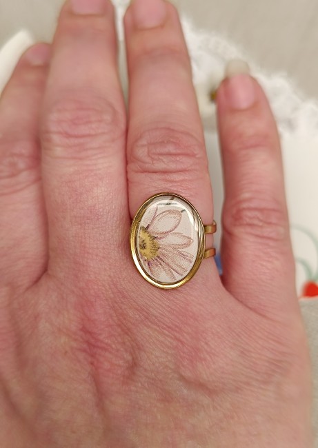 Bague présentée en main pour apprécier les dimensions du cabochon ovale et les détails du motif marguerite.