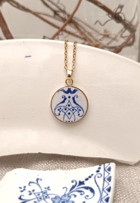 Photo du collier en faïence de Moustiers tenu dans les mains. Pièce unique façonnée à partir d’une assiette fendue. Bijou artisanal durable et poétique.
