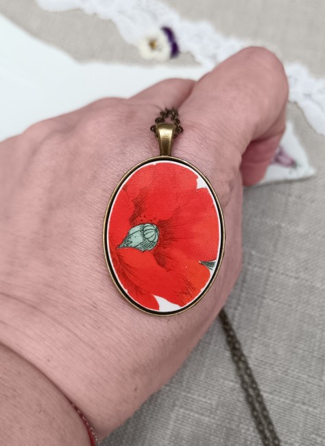Collier présenté en main pour apprécier les dimensions du pendentif ovale et les détails du motif floral