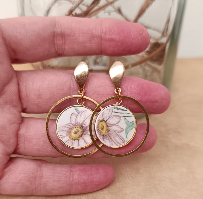 Boucles d'oreilles présentées en main pour apprécier les cabochons ronds de 20 mm et les détails du motif marguerite.