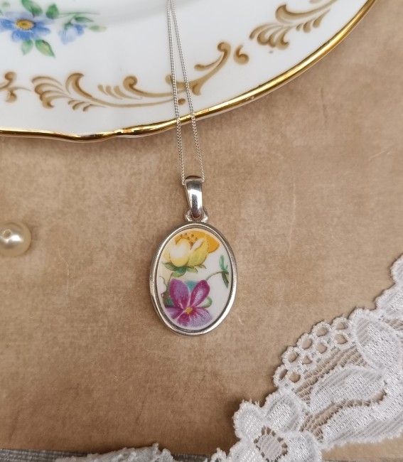 Collier POÉSIE tenu dans la main, détail du motif floral en porcelaine fine Crown Staffordshire, bijou poétique artisanal fabriqué en France.
