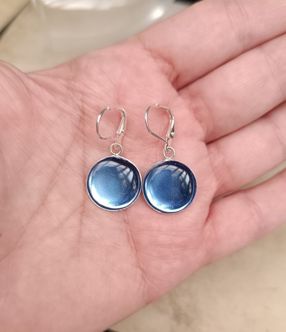 Boucles en verre bleu présentées en main pour visualiser leurs cabochons ronds de 16 mm et leurs proportions.