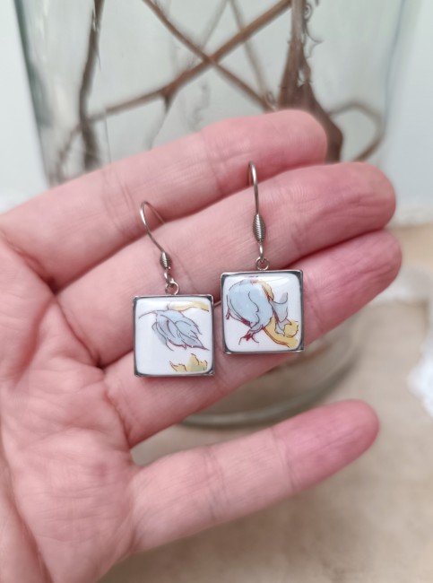 Boucles OPUS présentées en main pour apprécier leur format carré de 15 × 15 mm inspiré des tesselles de mosaïque.