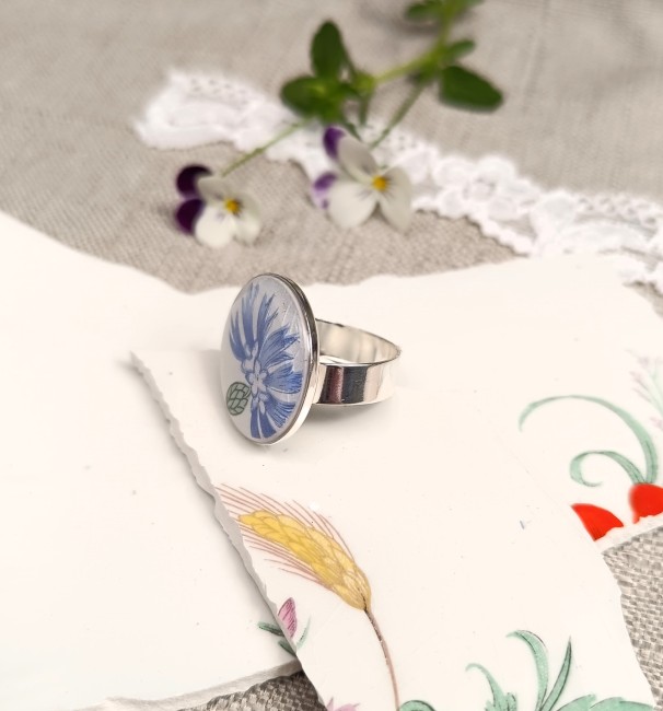 Grande bague présentée en main pour apprécier les dimensions du cabochon rond de 22 mm et les détails du motif bleuet.