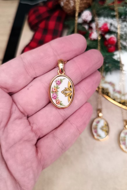 Collier porcelaine héritage – Taille et texture en main Collier artisanal présenté dans la main pour montrer la taille et la texture du pendentif en porcelaine familiale. Bijou ovale plaqué or, création française.