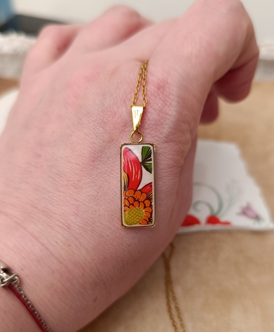 Collier Samba présenté en main pour apprécier les dimensions du pendentif rectangulaire et les détails du motif floral.
