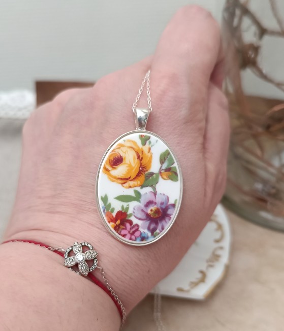 Collier POÉSIE tenu dans la main, détail du motif floral en porcelaine fine Crown Staffordshire, bijou poétique artisanal fabriqué en France.