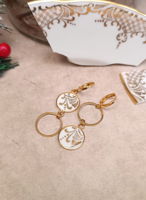 Découvrez les boucles d’oreilles Orion, pièce unique en porcelaine de Limoges recyclée, posées pour montrer le motif blanc et doré du bord d’assiette.