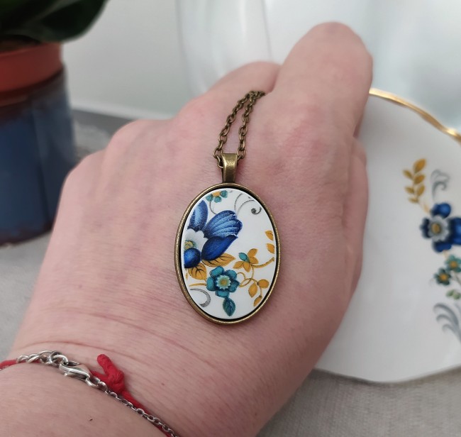 Collier MINI BROKEN SAPHIR tenu dans la main, détail du motif floral sur faïence Moulin des Loups, bijou artisanal français fait main.