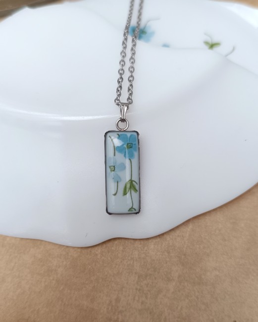 Collier Myosotis rectangulaire en acier inoxydable doré sur fond blanc.