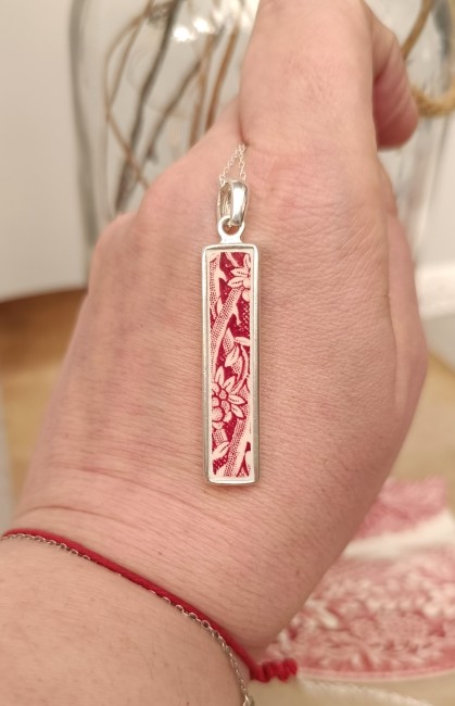 Collier SIROPI tenu dans la main, détail du motif en porcelaine anglaise rouge et blanche, création artisanale française unique.