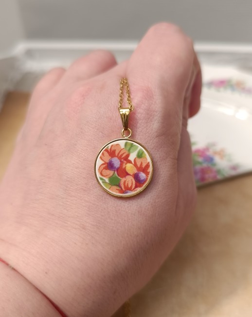 Collier présenté en main pour apprécier les dimensions réelles et les détails du décor floral.