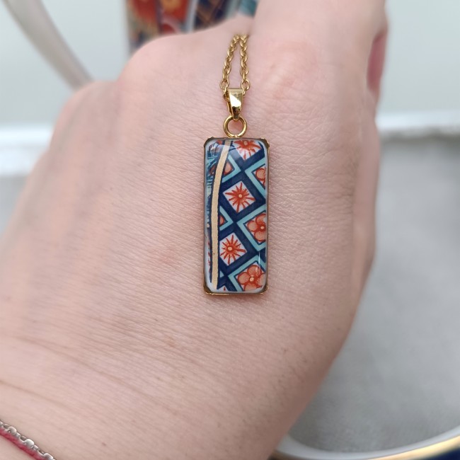Collier en porcelaine japonaise ancienne présenté en main pour visualiser son pendentif rectangulaire de 10 × 30 mm.