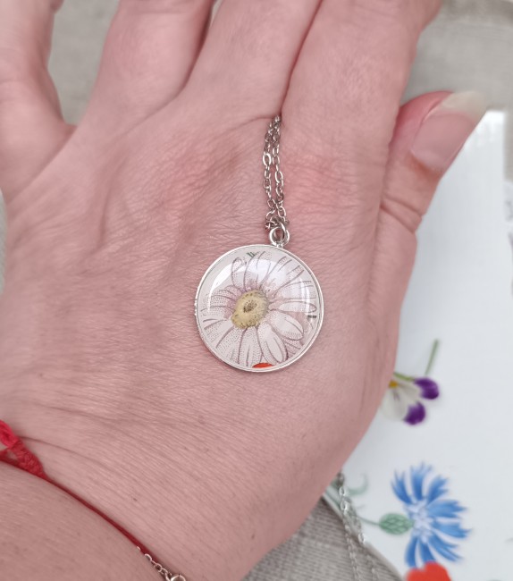 Collier présenté en main pour apprécier les dimensions du pendentif et la finesse du motif marguerite.