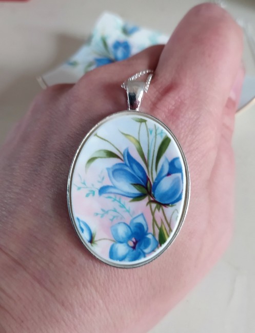 Collier Royal Tara tenu dans la main, détail du motif fleuri sur porcelaine irlandaise, bijou artisanal français fait main.