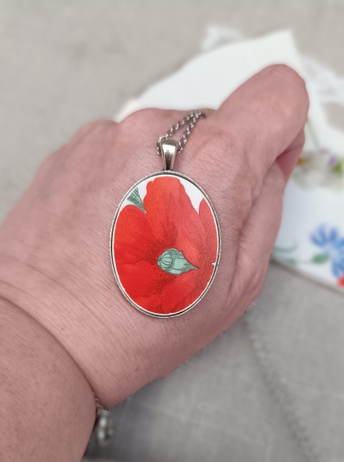 Collier présenté en main pour apprécier les dimensions du pendentif ovale et les détails du motif coquelicot.